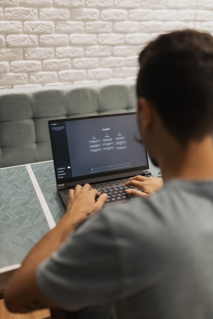 A man interacts with a laptop displaying the ChatGPT system indoors, focusing on technology.